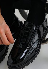 Pantofi din piele lacuită negri, cu un design cu șiret, închidere cu fermoar lateral și o talpă chunky. Textură netedă, cu minimalisme.