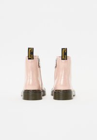 Botines de charol rosa con un acabado brillante, que cuentan con un cierre lateral de cremallera y una pestaña de tela con texto amarillo, suela negra en contraste.