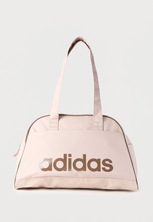 Rožnata torba iz tkanine z bež ročaji; na njej je velik bronast napis "adidas". Gladek tekstura, zaobljena oblika, zapiranje z zadrgo in poudarjeno šivanje.