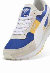 Puma sporta apavi ar zilu sietu un beigu zamšu, ar dzeltenām un baltām akcentiem. Biezas baltas šņores un teksturēta zole.