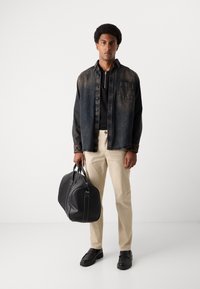 Denim jacket in dark wash, black turtleneck, beige trousers, holding a black leather bag. Outfit features minimal accents and structured design.