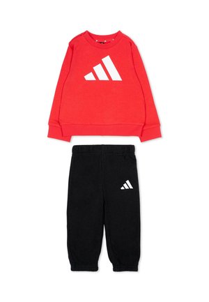 Czerwona bluza z długim rękawem oraz czarne spodnie dresowe z elastycznym pasem i białym logo Adidas na obu elementach, ułożone na płasko na białym tle.