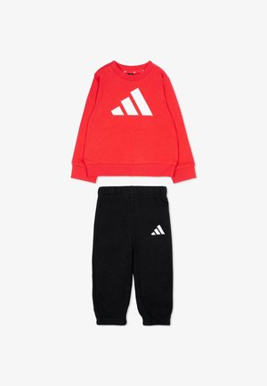 Felpa rossa a maniche lunghe e pantaloni da ginnastica neri con vita elastica e logo bianco Adidas su entrambi i capi, sistemati in piano su sfondo bianco.