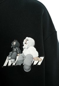 Dos figuras de dibujos animados con chaquetas con capucha, sentadas de espaldas sobre un fondo de tela negra con texto estilizado en blanco.