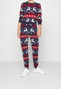 Marinblå jultröja och byxset med vita renar och röda hjärtan. Stickat material med ribbade muddar och midjeband. Vita sneakers.