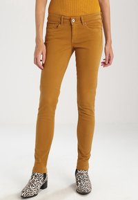 Mustard-colored skinny jeans made of a smooth fabric, featuring a classic five-pocket design and a front button closure. Pairing with leopard print ankle boots.