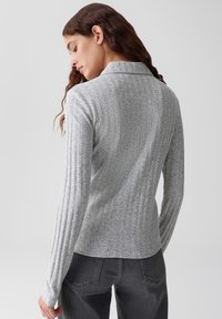 Maglione grigio a maniche lunghe a costine con colletto, caratterizzato da un tessuto testurizzato. Progettato con una silhouette aderente e orlo dritto in vita.