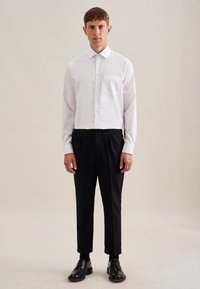 Witte button-up blouse met een borstzak, gecombineerd met zwarte taps toelopende broek en zwarte leren schoenen. Gladde textuur, klassiek ontwerp.
