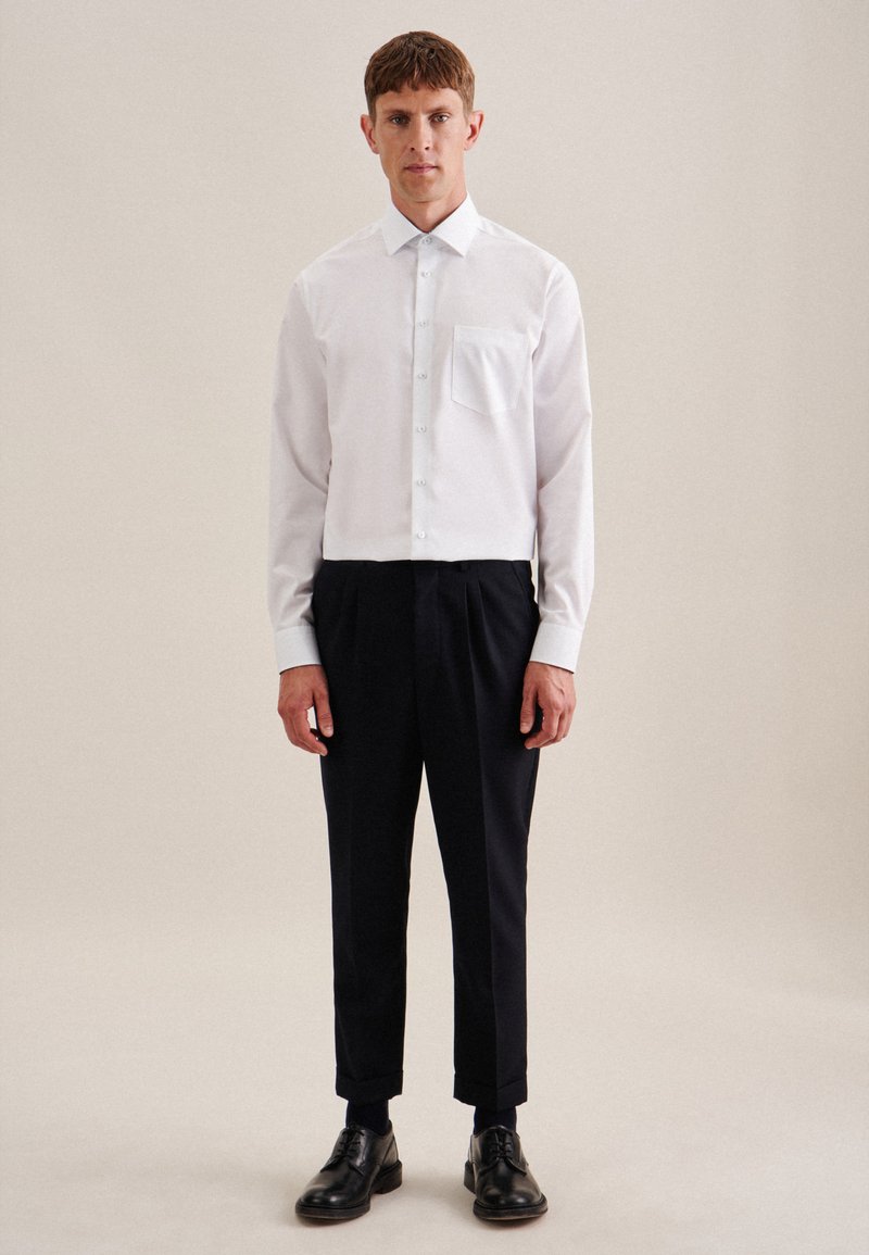 Witte button-up blouse met een borstzak, gecombineerd met zwarte taps toelopende broek en zwarte leren schoenen. Gladde textuur, klassiek ontwerp.