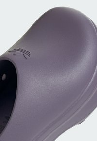 Zueco de goma púrpura con una superficie lisa y texturizada y una puntera redondeada. Presenta un acento con logo y un diseño de talón abierto para facilidad al usar.