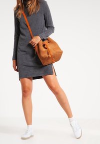Abito grigio a coste con maniche lunghe, caratterizzato da spacchi laterali. Borsa in suede marrone con tracolla arancione, abbinata a sneaker bianche.