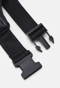 Czarny regulowany pasek wykonany z teksturowanego nylonu z plastikową klamrą. Klamra posiada logo oraz bezpieczny mechanizm blokujący.