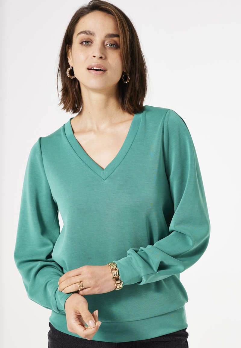 Haut à manches longues en V, de couleur teal uni, fabriqué à partir d'un tissu lisse et léger. Présente des manches froncées et un ourlet ajusté.