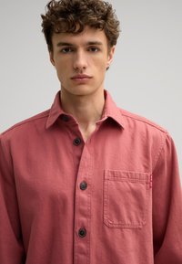 Korte mouwen, roze, knopsluiting shirt van katoen, met een voorktas, donkere knopen en een klein merketiket aan de zijkant.