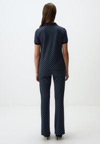 Marineblauwe gepolijste polo en uitlopende broek outfit. Heeft korte mouwen, een kraag en een gestructureerd ontwerp tegen een effen achtergrond.