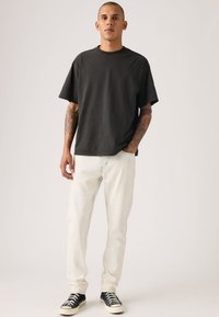 Μαύρο κοντομάνικο μπλουζάκι με στρογγυλή λαιμόκοψη, συνδυασμένο με ανοιχτόχρωμο τζιν και μαύρα αθλητικά παπούτσια με λευκές λεπτομέρειες.