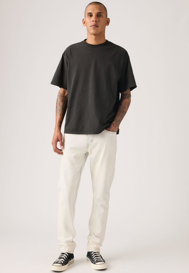 T-shirt noir à manches courtes avec un col rond, associé à un jean clair et des baskets noires avec des accents blancs.