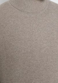 Zbliżenie beżowego swetra z golfem, ukazujące teksturę materiału i szczegóły prążkowanego kołnierza.