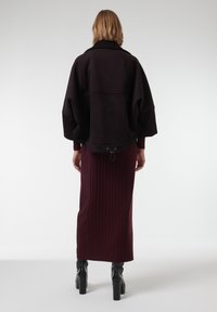 Chaqueta negra de gran tamaño con cuello alto; falda de canalé burdeos y botas negras de tacón bloque. Detalle de cordón en el dobladillo de la falda.