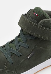 Zelene nubuk visoke tenisice s teksturiranim mrežastim unutrašnjim oblogom, ojačanim vrhom i čičak trakama; s GORE-TEX logotipom i gumenim potplatom.