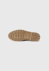 Suela de zapato de goma color beige con un patrón rugoso que presenta surcos profundos y tracción multidireccional para estabilidad y agarre.