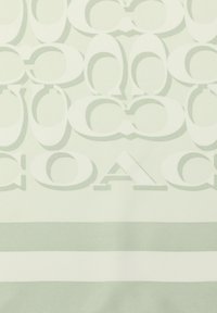 Tessuto decorato con motivi ripetuti di forme "C" intrecciate e la parola "COACH" in colori verde chiaro e crema con finitura strutturata.