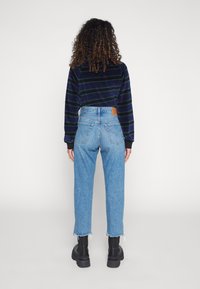 Jeans blu a vita alta con orlo sfrangiato, abbinati a un top a strisce blu navy a maniche lunghe. Stivali neri alla caviglia completano l'outfit.