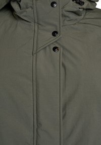 Podrobni posnetek sprednje strani olivno zelene jakne z črnimi pritrdilnimi gumbi in vidnim šivanjem na vodoodporni tkanini.
