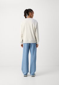 Ανοιχτό γκρίζο φούτερ με άνετη εφαρμογή, ριμπ μανσέτες, φορεμένο με χαλαρούς μπλε τζιν παντελόνες, ορατό ράψιμο και υφή υφάσματος.