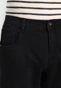 Zwarte denim jeans met een klassieke snit, voorzien van een voorkantzak en een knoopsluiting. De stof heeft een gladde textuur met minimale glans.