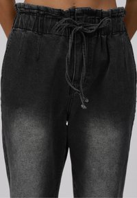 Pantalon en denim noir taille haute avec un effet délavé et un cordon en tissu noué en nœud papillon à la taille devant.