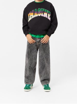 Sort sweatshirt med "IMAGINE" grafik i multicolorede tekst, grøn lagdelt skjorte, posede grå denim jeans og grønne sneakers.