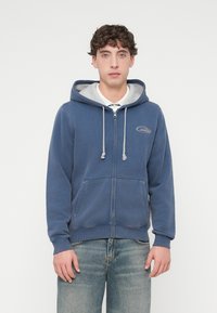 Μπλε φούτερ με φερμουάρ, γκρι εσωτερική επένδυση, κορδόνι και τσέπες μπροστά. Διαθέτει μικρό λογότυπο στο αριστερό στήθος. Μαλακή υφή υφάσματος.