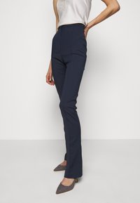 Pantalones de cintura alta en color marino con un corte ajustado. La tela tiene una textura suave. Combinados con tacones estampados que cuentan con un diseño de punta afilada.