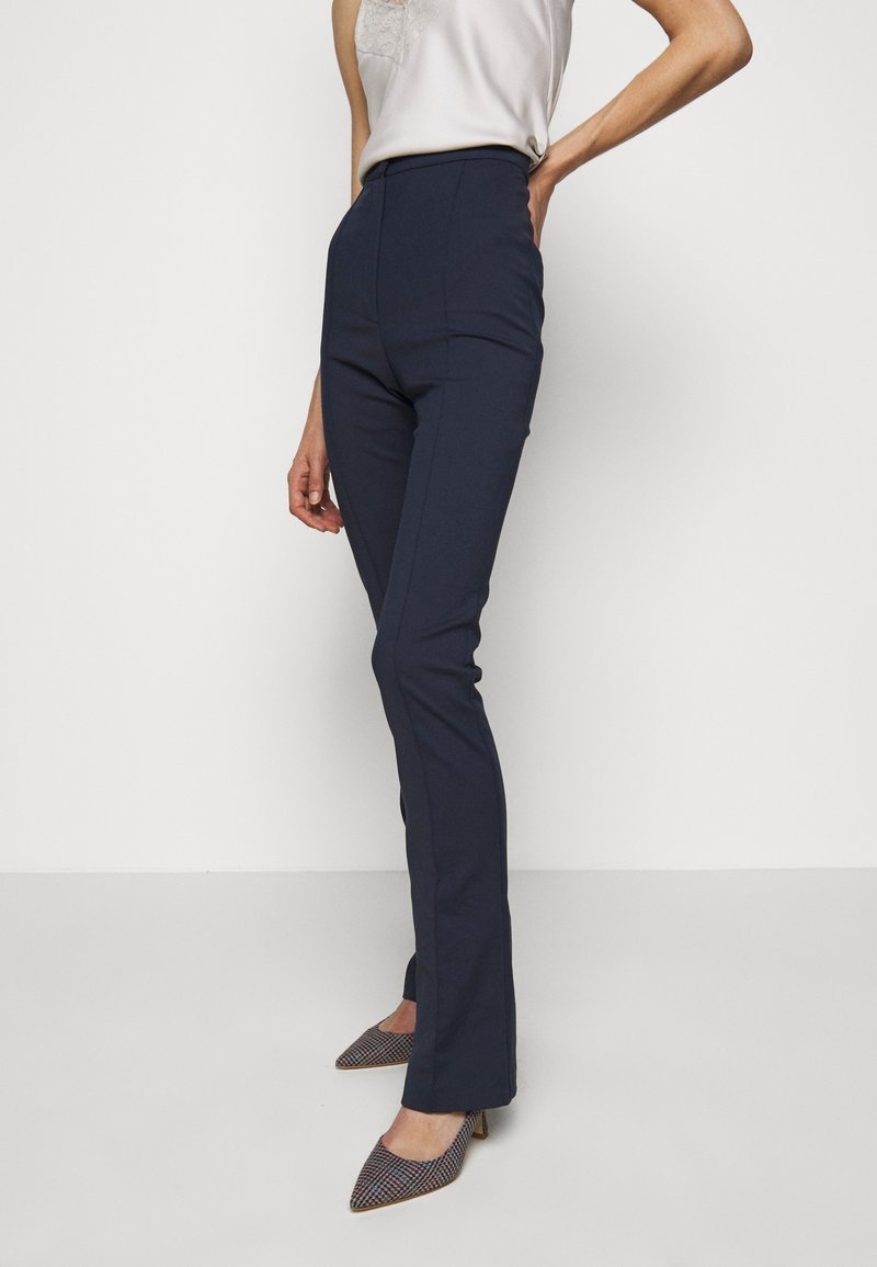 Pantalones de cintura alta en color marino con un corte ajustado. La tela tiene una textura suave. Combinados con tacones estampados que cuentan con un diseño de punta afilada.