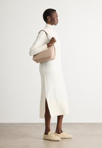 Robe en tricot crème avec un col haut et des fentes latérales, assortie à des baskets beige et un sac à main structuré rose clair. Texture lisse.