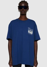 Blå bomulls-t-shirt med en avslappnad passform. Har en grafisk tryckt fickdesign med texten "HALO 196819721981" i vitt. Korta ärmar.