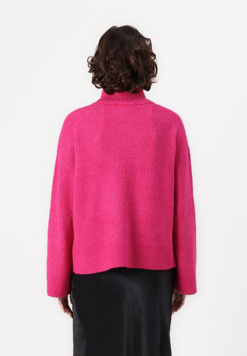 Fuksjowy sweter dzianinowy z wysokim kołnierzem, opadającymi ramionami i luźnym krojem. Teksturowane wykończenie z prążkowanym dołem, w zestawieniu z czarną spódnicą.
