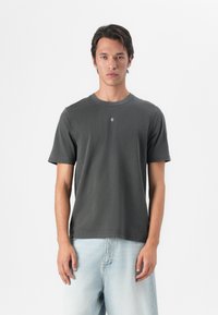Dunkelgraues Baumwoll-T-Shirt mit Rundhalsausschnitt, kurzen Ärmeln und einem kleinen Logodetail auf der Brust, kombiniert mit hellblauen Jeans.