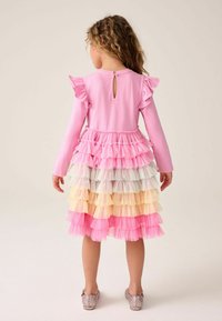 Ruža obleka z dolgimi rokavi in volančki na ramenih ter s plastevnim krilom v pastelnih barvah, z odprtinami na hrbtu in bleščečimi čevlji.