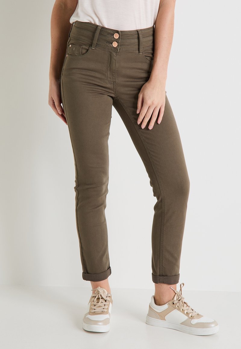 Jeans verde oliva de corte slim con cintura alta, con tres botones frontales y dobladillos enrollados, combinados con zapatillas beige y blancas.