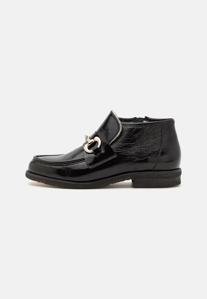 Botines de charol negro con punta redonda, herrajes decorativos de hebilla y un tacón bajo. Textura suave con un brillo sutil.