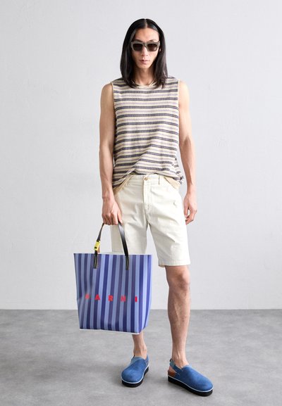 Sleeveless striped top in beige and navy, cream shorts, blue clogs, and a blue striped tote with red lettering. Neutral background.