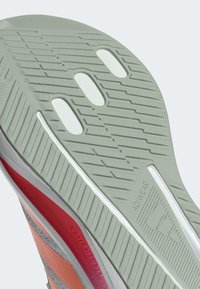 Suela de zapato con una base de goma verde y un patrón texturizado, acentos blancos y detalles rojos a lo largo de los lados, etiquetada "ADWEAR".