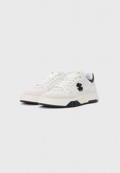 Valged madalad sneakers mustade aktsentidega, perfokaatoriga varbaosa, paelad ja tõstetud must logo külgedel, esitatud valgel taustal.