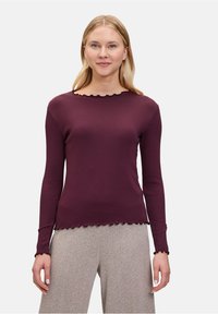 Haut à manches longues bordeaux avec un ourlet et un col en feston. Design ajusté avec une texture côtelée, associé à un pantalon à motifs gris clair.
