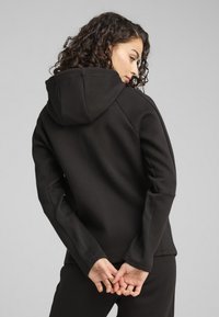 Sudadera con capucha negra de textura suave, forma ajustada y mangas largas, presenta costuras en contraste y una capucha relajada.