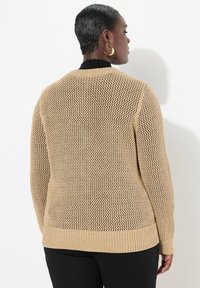 Maglione lavorato a maglia in un colore beige chiaro con una trama aperta simile all'uncinetto, orlo e colletto a costine. Il design presenta maniche lunghe e una vestibilità comoda.