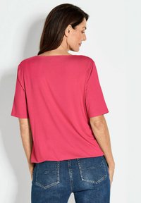Top rosa chiaro a maniche corte con scollatura ampia, abbinato a jeans in denim blu. I pantaloni presentano cuciture decorative sulle tasche posteriori.