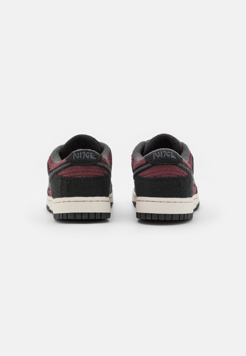 Ein Paar schwarze und dunkelrote Nike-Sneaker aus strukturiertem Stoff, von hinten auf einem weißen Hintergrund gezeigt.